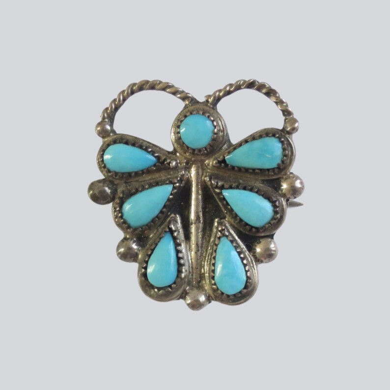 Retro 70s BoHo turquoise and silver butterfly brooch or pin measuring approximately 1 inch in diameter,  Shown in full close up with a gray background.