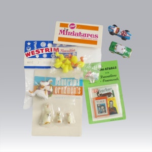 May include: A collection of miniature toys and ornaments, including small yellow rubber ducks, geese, and cars. Packages of miniatures with the text "Miniatures" and "Panorama Ornaments" are also visible.