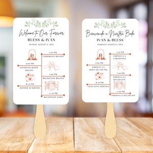 May include: Two white wedding fan programs with wooden handles. The fans feature a timeline of events, including ceremony, cocktail hour, and reception details. The text reads "Welcome to Our Forever" and "Bless & Ivan."