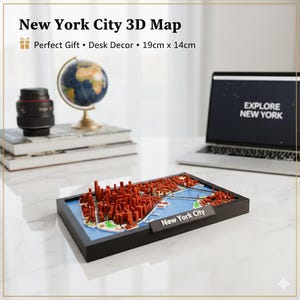 Può includere: Una mappa 3D di New York City, con edifici rossi e acqua blu, in una cornice nera. La mappa è etichettata "New York City" e misura 19cm x 14cm. Un laptop con "EXPLORE NEW YORK" sullo schermo è sullo sfondo.