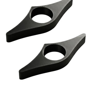 May include: Two black, 3D-printed book page holders. Each holder has a circular opening and a pointed end. The holders are designed to keep a book open. The holders are made of a textured material.