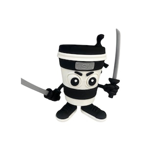 May include: A novelty coffee cup figurine designed as a ninja. The cup is white with black stripes, a black lid, and a black headband. It holds two grey swords and wears black shoes. The figurine has large, expressive eyes.