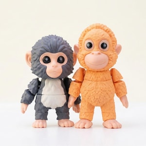 Peut inclure: Deux figurines de singes articulées, l'une grise et l'autre orange. La figurine grise a une poitrine blanche. Les deux singes ont de grands yeux expressifs et des membres articulés. Les figurines présentent des détails réalistes et une texture.