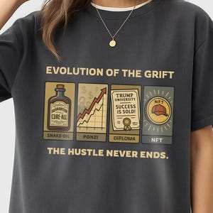 May include: Dark grey t-shirt featuring the text "EVOLUTION OF THE GRIFT" and illustrations of a snake oil bottle, a rising graph, a diploma, and an NFT. The phrase "THE HUSTLE NEVER ENDS" is printed below the illustrations.