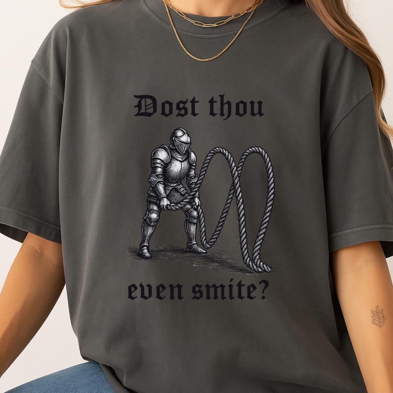 Puede incluir: Camiseta gris oscuro con el texto "Dost thou even smite?" encima y debajo de una ilustraci&oacute;n en blanco y negro de un caballero con armadura sosteniendo una cuerda.
