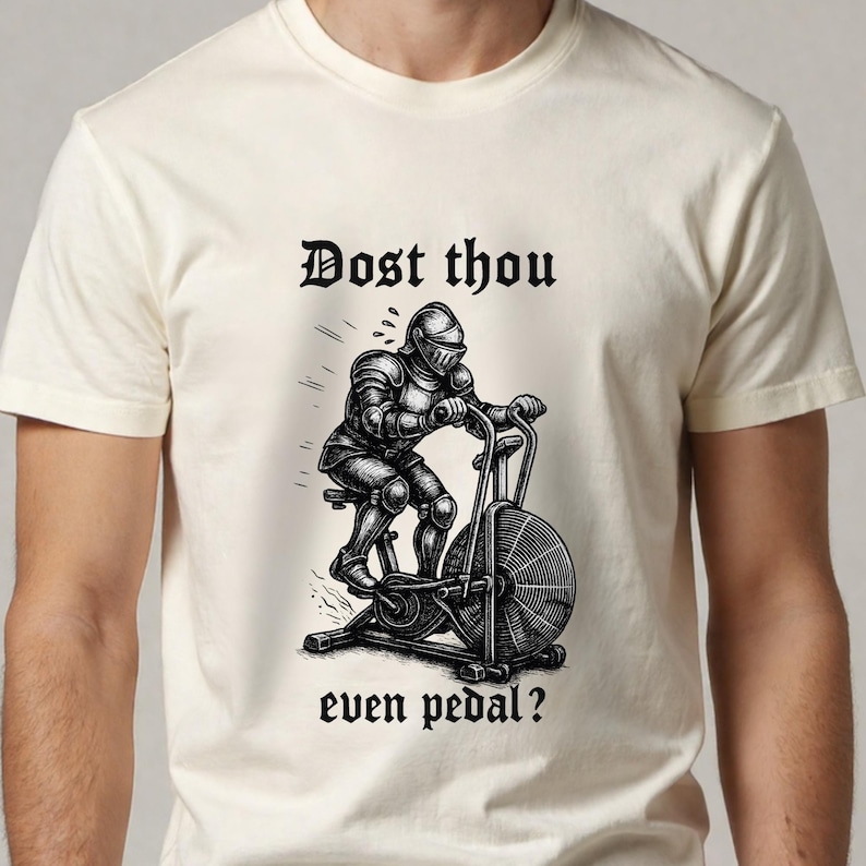 May include: Cream-colored t-shirt featuring a black and white illustration of a knight in full armor riding an exercise bike. The text "Dost thou even pedal?" is above and below the image.