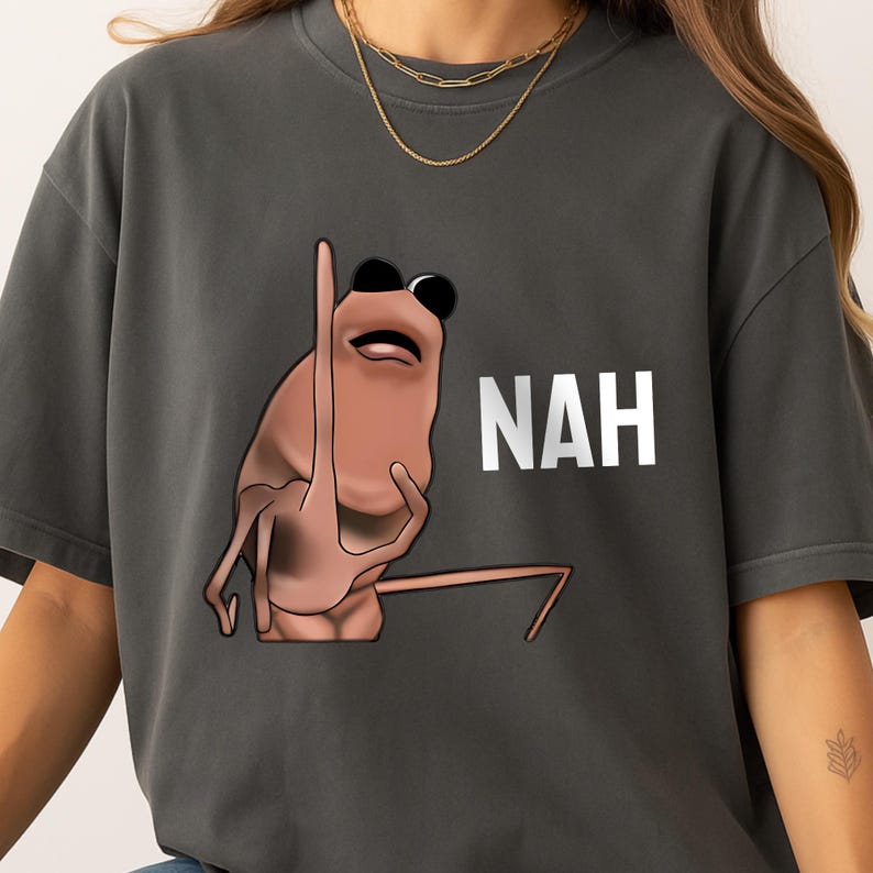 Op de afbeelding: Donkergrijs T-shirt met een cartoon garnaal met een zonnebril en het woord "NAH" in het wit. De garnaal is lichtbruin en heeft een ontspannen houding. Het T-shirt is een casual stijl.