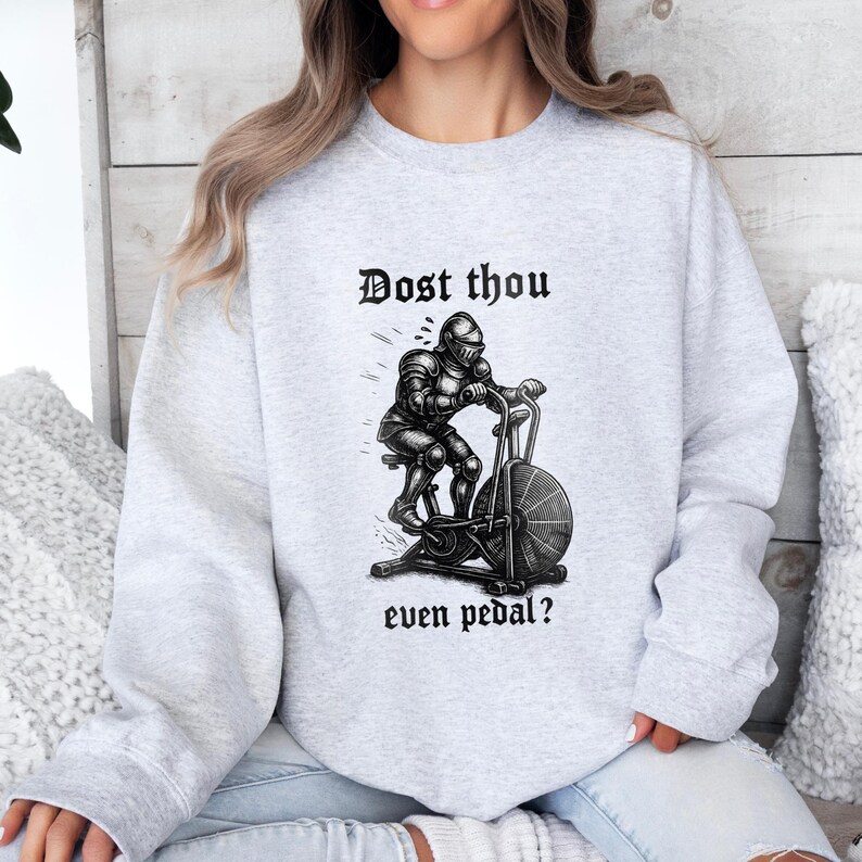 May include: Light gray sweatshirt with the text "Dost thou even pedal?" above a black and white illustration of a knight on an exercise bike. The sweatshirt is a crew neck style.