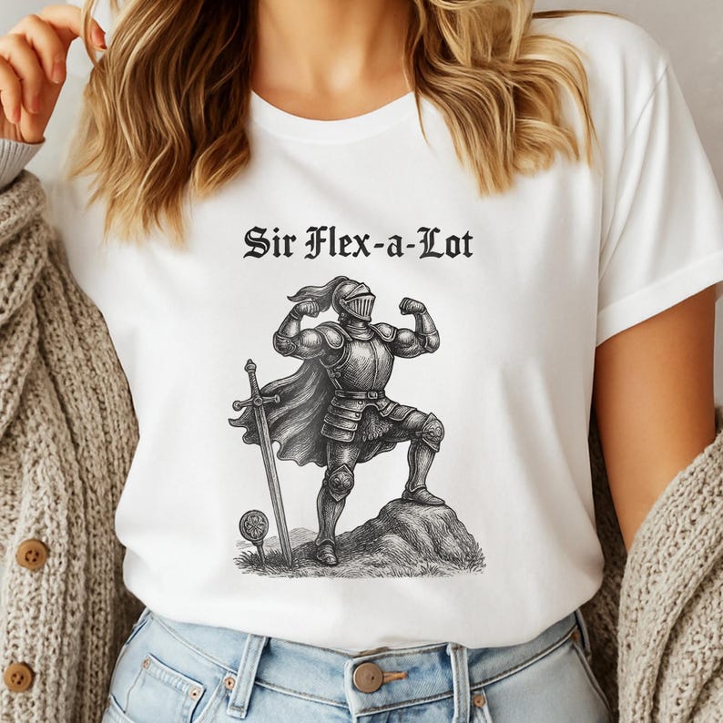 Pu&ograve; includere: T-shirt bianca con la scritta "Sir Flex-a-Lot" sopra un'illustrazione dettagliata di un cavaliere muscoloso in armatura. Il cavaliere &egrave; in piedi su una roccia con una spada e una pallina da golf. Il disegno &egrave; in bianco e nero.