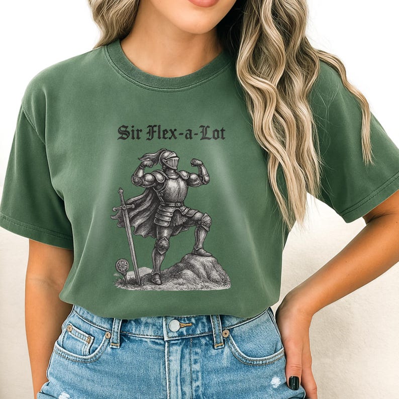 Pu&ograve; includere: T-shirt verde con la scritta "Sir Flex-a-Lot" e un'illustrazione in bianco e nero di un cavaliere in armatura che mostra i suoi muscoli. Il cavaliere &egrave; in piedi su una roccia con una spada. La maglietta &egrave; abbinata a jeans blu.