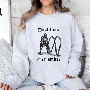 Puede incluir: Sudadera gris claro con el texto "Dost thou even smite?" encima y debajo de una ilustraci&oacute;n en blanco y negro de un caballero con armadura tirando de una cuerda.