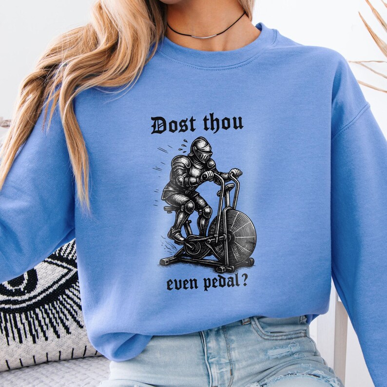 May include: Light blue sweatshirt with a black and white graphic of a knight on an exercise bike. The text "Dost thou even pedal?" is printed above and below the graphic in a gothic font.