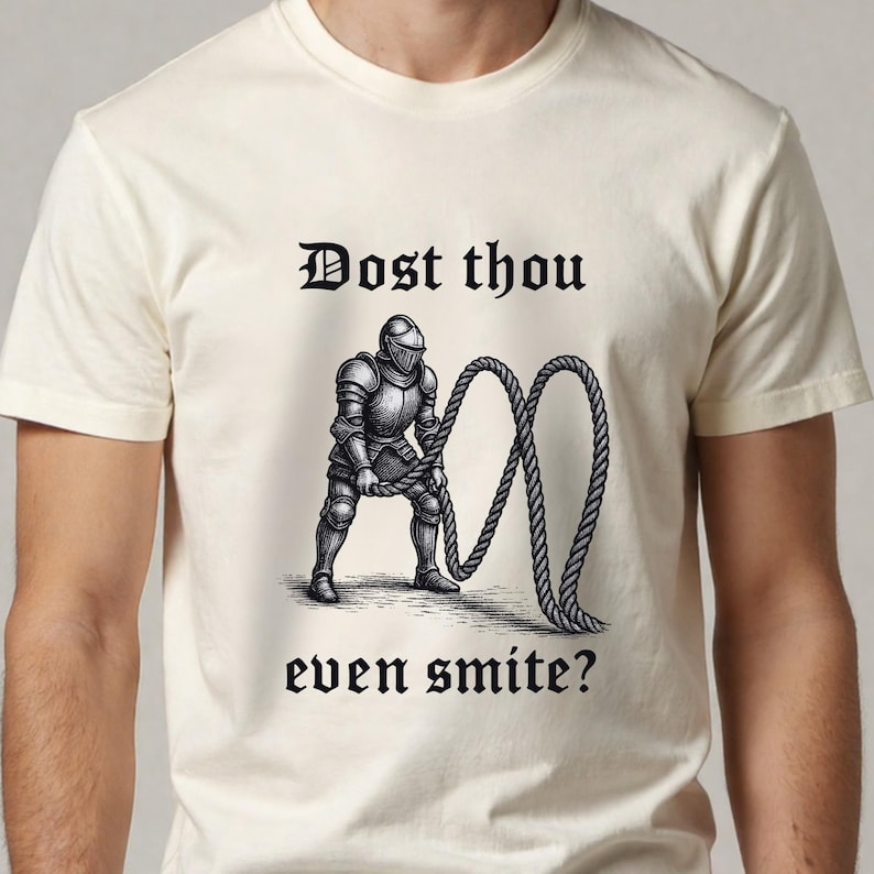 Puede incluir: Camiseta color crema con una ilustraci&oacute;n negra de un caballero sosteniendo una cuerda, con el texto "Dost thou even smite?" en fuente g&oacute;tica. El dise&ntilde;o est&aacute; centrado en la camiseta.