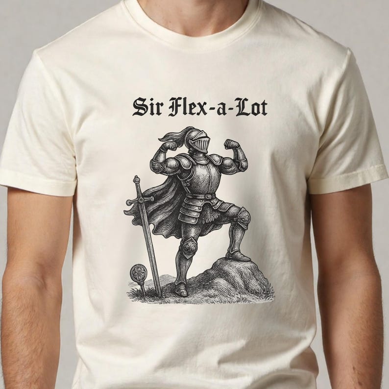 Pu&ograve; includere: T-shirt color crema con un'illustrazione nera di un cavaliere muscoloso in armatura, una spada e la scritta "Sir Flex-a-Lot" in carattere gotico. Il cavaliere &egrave; in piedi su una roccia.