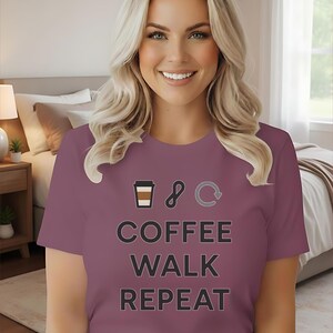 May include: Berry-coloured t-shirt with the text "COFFEE WALK REPEAT" and related graphics. The shirt features a coffee cup, infinity symbol, and a circular arrow. The model is wearing blue jeans.