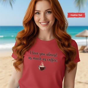 May include: A red t-shirt with the text "I love you almost as much as coffee" and a coffee cup graphic. The shirt is worn by a person with long red hair. The background shows a beach scene.