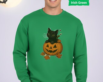 Könnte beinhalten: Irisch grünes Sweatshirt mit einer schwarzen Katze in einem geschnitzten Kürbis. Der Kürbis hat ein lächelndes Gesicht und ist von Herbstblättern umgeben. Der Hintergrund zeigt einen Vollmond und Fledermäuse, was ein Halloween-Thema erzeugt.