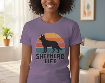 May include: Violet t-shirt with a graphic of a German Shepherd dog silhouette against a sunset design. The text "SHEPHERD LIFE" is below the dog. The shirt is being worn.