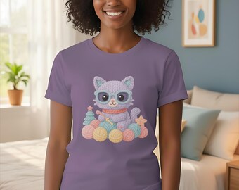 May include: A violet t-shirt featuring a cartoon cat wearing glasses and a scarf, surrounded by yarn balls and a small Christmas tree. The cat is light purple with blue accents. The word "Violet" is at the bottom of the image.