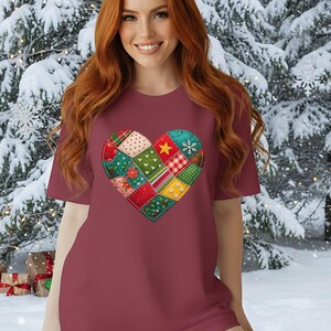 May include: Crimson t-shirt with a patchwork heart design. The heart features diverse fabric patterns, including polka dots, stripes, and floral prints, with a yellow star and snowflake. The shirt is set against a snowy winter backdrop.