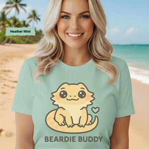 Puede incluir: Camiseta verde claro con un diseño de dragón barbudo de dibujos animados y el texto "BEARDIE BUDDY". La camiseta es de color menta brezo.