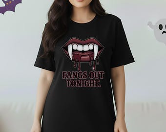 May include: Black t-shirt dress with a vampire fangs graphic and the text "Fangs Out Tonight." The design features a pair of red lips with dripping blood and sharp white fangs. The dress is a casual, short-sleeved style.