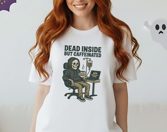 May include: White t-shirt with the text "DEAD INSIDE BUT CAFFEINATED" and a cartoon skeleton graphic. The skeleton is seated at a desk with a laptop and IV drip. Halloween decorations are in the background.