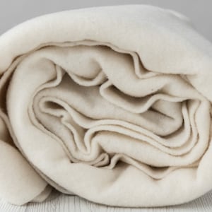 May include: A close-up of a rolled up, off-white, natural wool felt fabric. The fabric is soft and has a slightly textured surface.