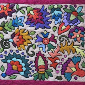 May include: A colorful felt wall hanging with a floral design. The flowers are in shades of red, orange, yellow, green, blue, and purple. The background is a light beige color and the border is a deep pink.
