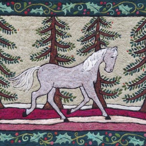 May include: A handcrafted textile art piece featuring a white horse walking through a forest of evergreen trees. The horse is depicted in profile, with a flowing mane and tail. The artwork is framed with a green border adorned with holly and berries.