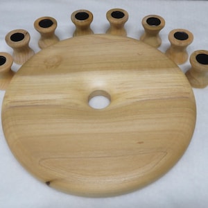 May include: A light brown wooden circular base with a central hole, surrounded by eight small, matching wooden candle holders. Each holder features a smooth, natural wood grain finish and a dark, circular interior opening for a candle.