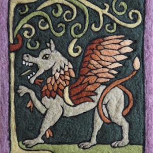 May include: A felt wall hanging with a green background and a stylized image of a winged creature with a long tail. The creature is brown, orange, and white. The background is decorated with green and yellow vines.