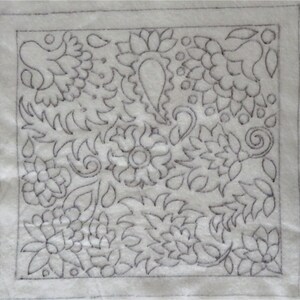 May include: A white fabric square with a black outline and a detailed floral design embroidered on it.