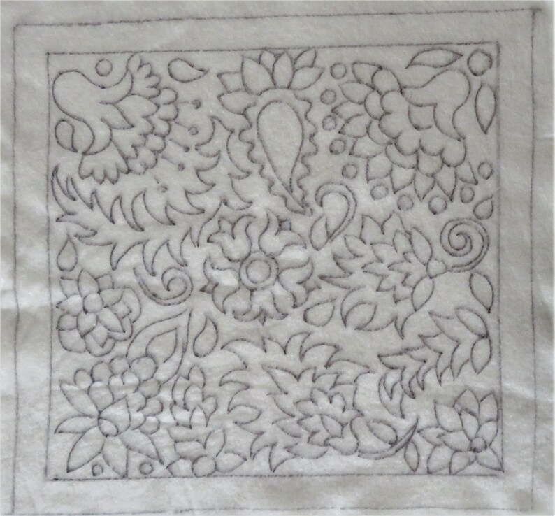 May include: A white fabric square with a black outline and a detailed floral design embroidered on it.
