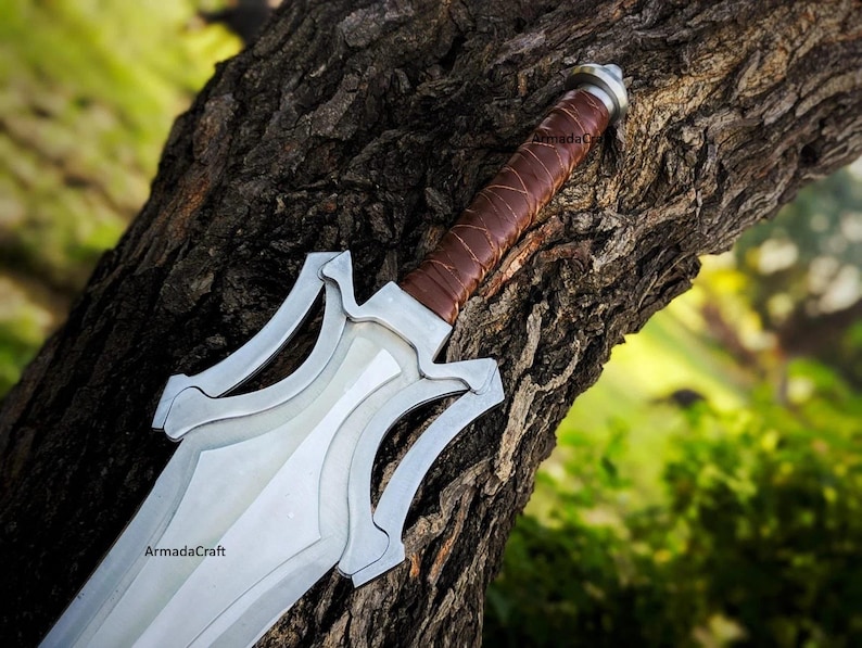 May include: A silver and brown sword with a leather-wrapped handle rests against a tree trunk. The blade is silver with a decorative design. The handle is brown leather. The sword is a fantasy-themed item.