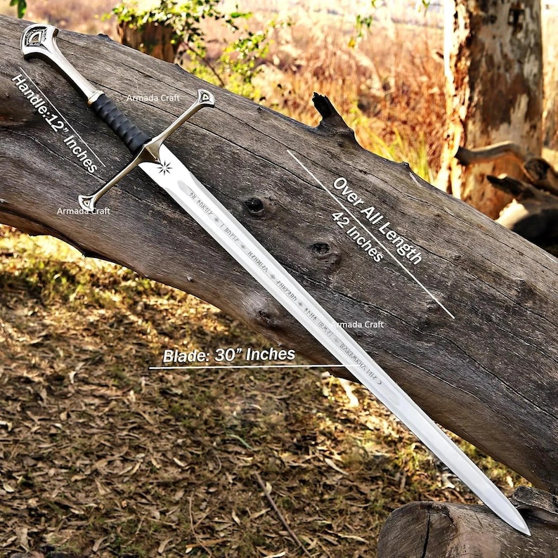May include: A silver sword with a 30-inch blade, 12-inch handle, and a total length of 42 inches. The sword features a black handle grip and ornate silver crossguard and pommel. The blade has engraved text. The sword is displayed on a weathered log.
