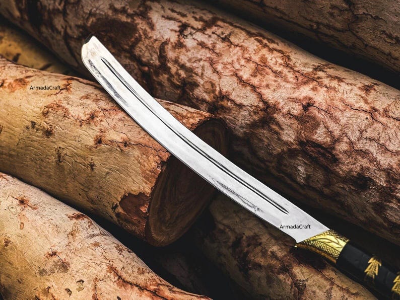 May include: A curved, silver blade sword with a black and gold handle. The blade has a central groove and is set against a backdrop of textured, brown wooden logs. The sword's handle features intricate gold detailing.