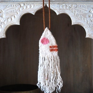 May include: A white woven wall hanging with a pink and orange geometric design. The hanging has a fringe at the bottom and is strung on a brown cord.