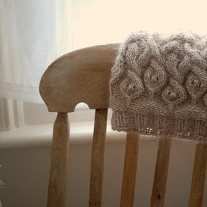 May include: A beige knitted scarf with a cable knit pattern draped over a wooden chair.