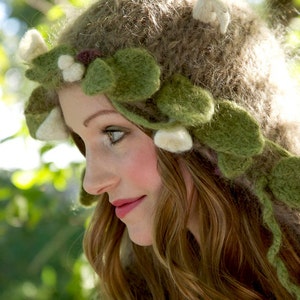 May include: A whimsical, handmade hat with a nature-inspired design. The hat is primarily brown with green felt leaves and white accents. The design evokes a woodland or fairy theme, perfect for costume or themed events.