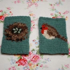 Könnte beinhalten: Zwei gestrickte fingerlose Handschuhe in Tealblau mit einem Rotkehlchen- und einem Vogelnester-Design.