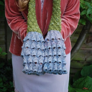 May include: A blue and green knitted scarf with a unique textured design. The scarf is made of soft yarn and has a delicate, feminine feel.