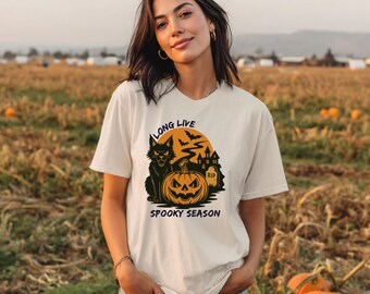 May include: Cream-colored t-shirt with a Halloween-themed graphic. The design features a black cat, jack-o'-lantern, bats, and a haunted house against an orange moon. The text reads "LONG LIVE" and "SPOOKY SEASON".