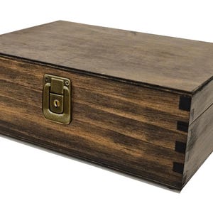 May include: A rectangular wooden box with a dark brown stain. The box has a metal clasp and hinges. The corners of the box are joined with dovetail joints. The box is sitting on a white surface.