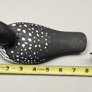 May include: Two wooden loon decoys, one large and one small, are displayed on a white surface. The larger decoy is approximately 10 inches long, and the smaller one is about 4 inches long. Both are painted black with white spots.