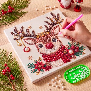 May include: A square diamond painting kit featuring a cartoon reindeer with a red nose, wearing a red scarf, surrounded by poinsettia flowers and snowflakes. The design is composed of small, colorful beads applied to a canvas surface.