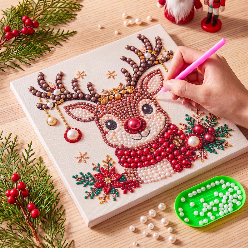 May include: A square diamond painting kit featuring a cartoon reindeer with a red nose, wearing a red scarf, surrounded by poinsettia flowers and snowflakes. The design is composed of small, colorful beads applied to a canvas surface.