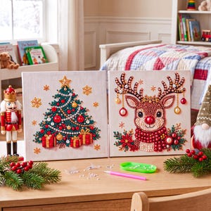 May include: Two square diamond painting canvases featuring Christmas themes. One canvas displays a decorated green Christmas tree with red ornaments and gifts. The other canvas shows a reindeer with antlers adorned with ornaments and poinsettias.