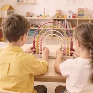 May include: Two children are seated at a wooden table, interacting with a colorful wooden rainbow abacus. The abacus features red, yellow, and pink arches with wooden beads. The word "shine" is visible on the abacus. The children are in a brightly lit room.