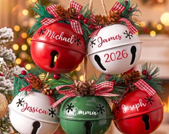 May include: Five round metal jingle bell ornaments in red, white, and green. Each bell features a name in script font, including Michael, James, Jessica, Emma, and Joseph, with the year 2026 on one. Topped with pine needles, pinecones, and red plaid bows.